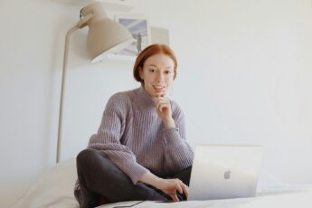 Eine junge Frau mit Laptop lacht in die Kamera, da sie für ihre Zukunft vorgesorgt hat, indem sie Festgeld angelegt hat.