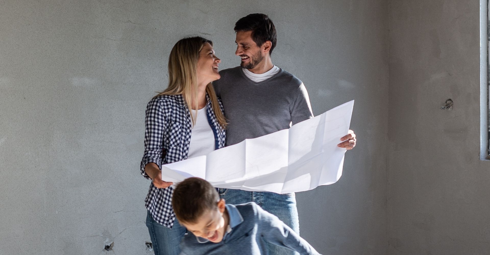 Junge Familie in Rohbau mit Plan in der Hand.