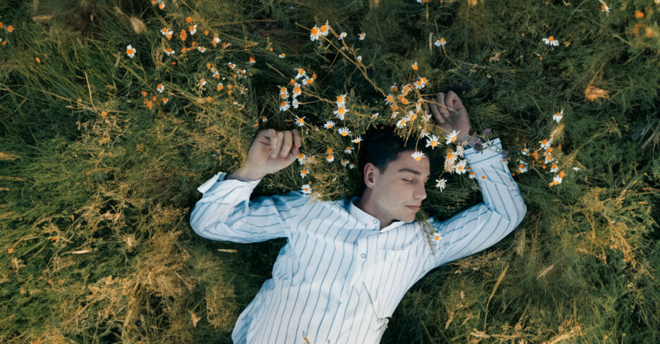 Mann in gestreiftem Hemd liegt entspannt auf einer Wiese mit Blumen – symbolisch für nachhaltiges & entspanntes Investment.