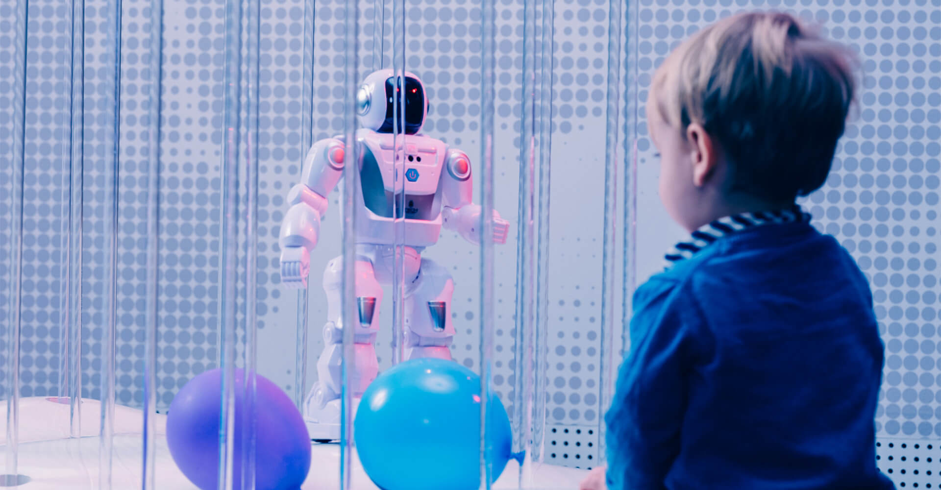 Ein Kind betrachtet neugierig einen humanoiden Roboter hinter Glas – Begegnung von Mensch und Technologie.