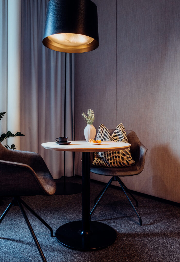 Ein moderner Tisch mit zwei Stühlen, einer Vase & einer Tasse, beleuchtet von einer großen Deckenlampe in einem stilvollen Raum.