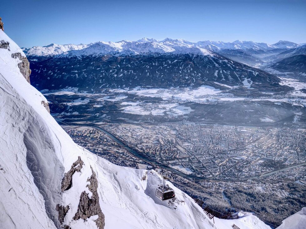 Die Aussicht von der Nordkette in die Stadt Innsbruck & das umliegende Bergland mit schneebedeckten Gipfeln.