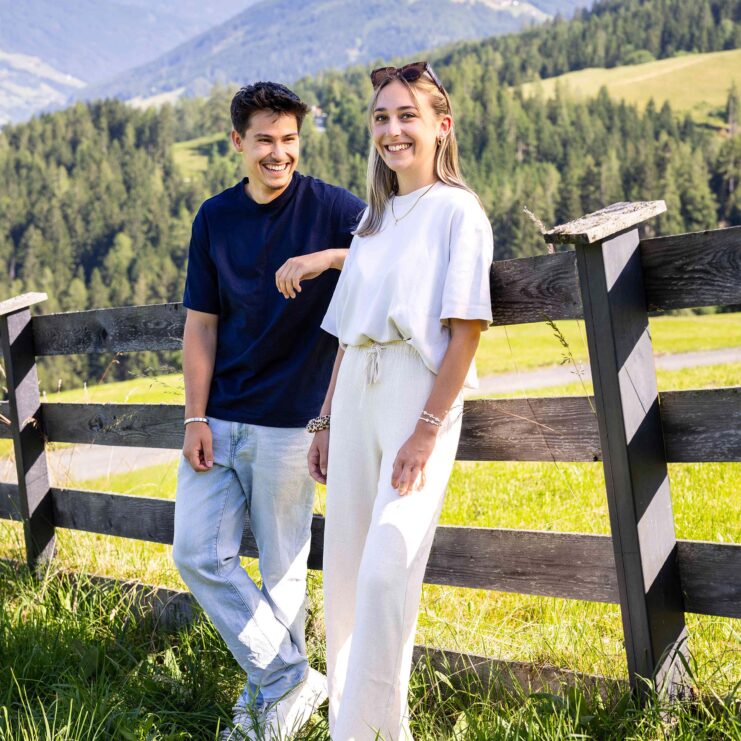 Zwei junge Menschen stehen angelehnt an einen Zaun und lachen.