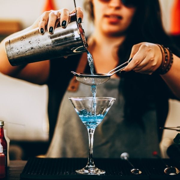 Barkeeperin gießt einen blauen Cocktail in ein Glas, Nahaufnahme beim Mixen.