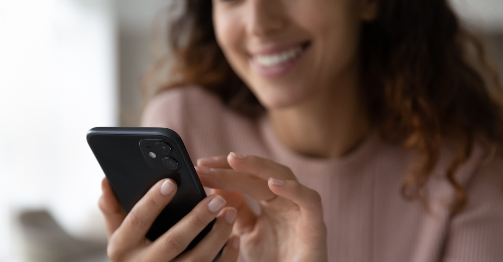 Frau tippt lächelnd auf ihr Smartphone.