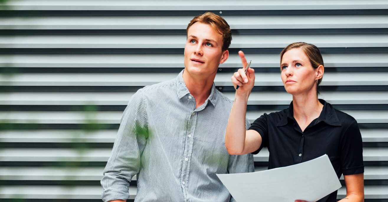 Zwei Berufstätige mit Laptop vor moderner Fassade – Austausch und Planung im Berufsalltag.