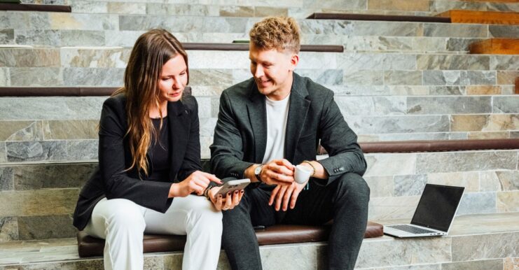 Kolleg:innen sitzen auf Stufen, besprechen Unterlagen und arbeiten am Laptop – Beratungssituation.