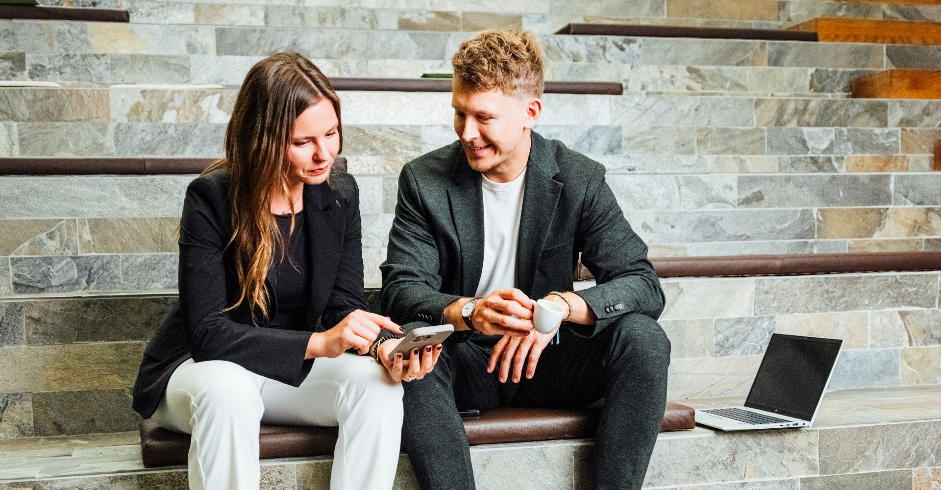 Kolleg:innen sitzen auf Stufen, besprechen Unterlagen und arbeiten am Laptop – Beratungssituation.