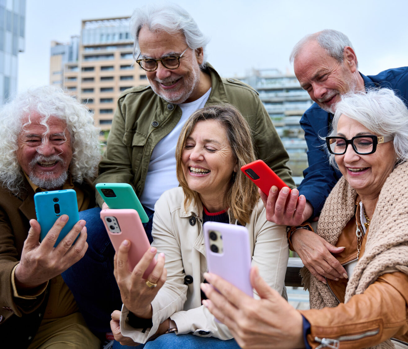 Gruppe älterer Menschen lacht gemeinsam und blickt auf ihre Smartphones – Freude an digitaler Vernetzung und Technik