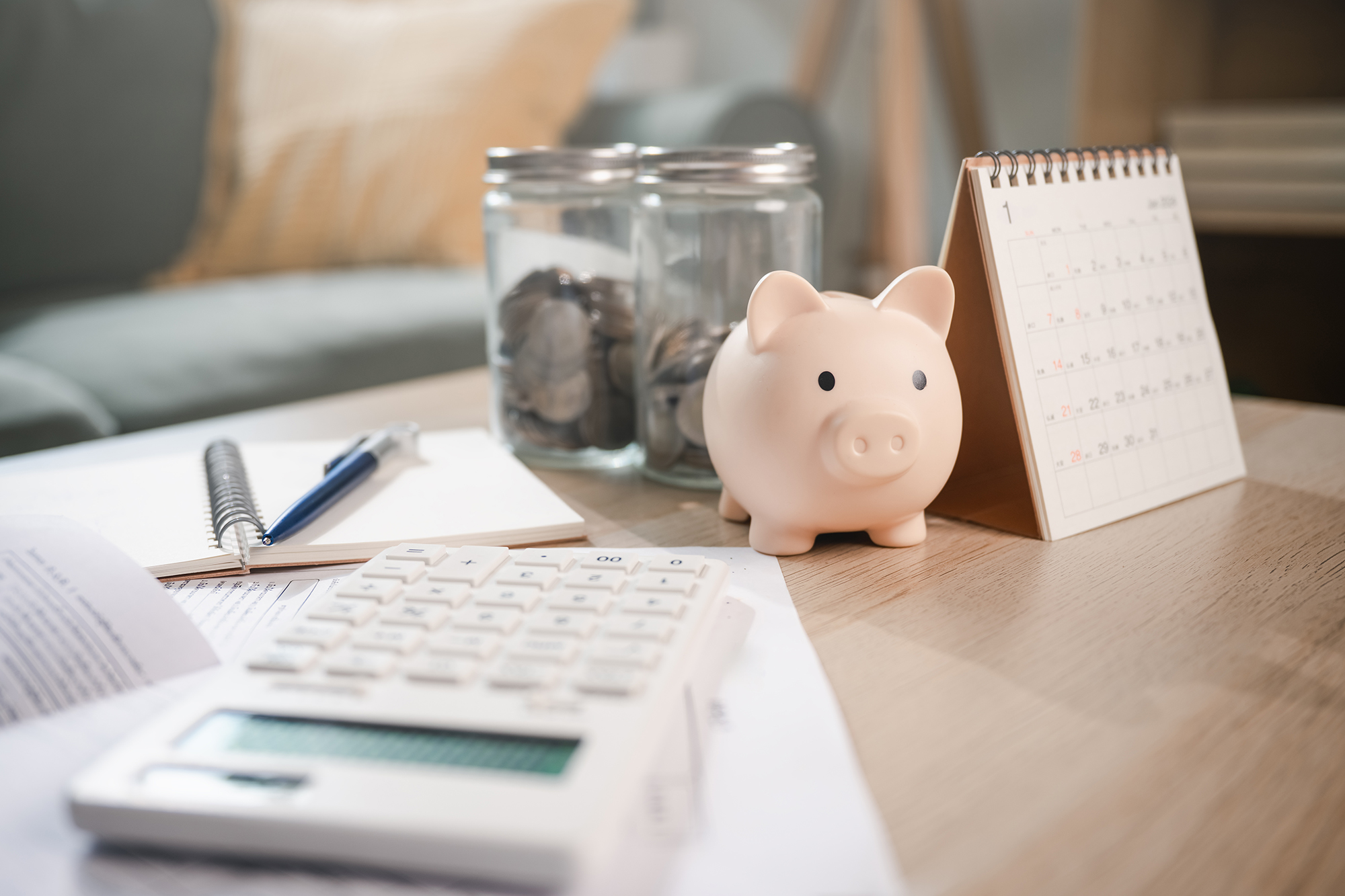 Spardose, Kalender, Münzgläser und Taschenrechner auf einem Tisch – Symbol für geplante, sichere und langfristige Geldanlage
