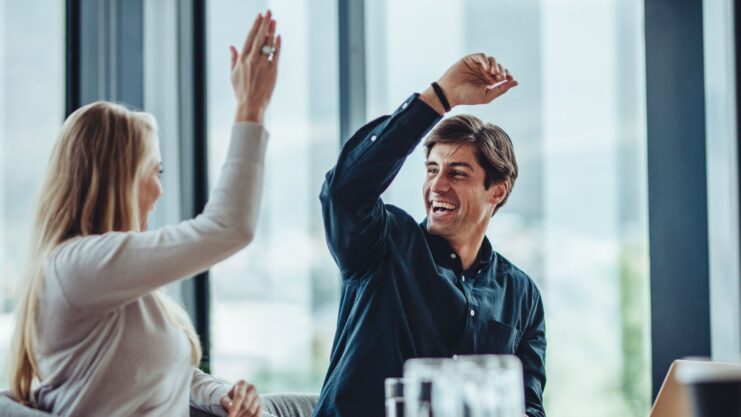 Zwei Personen geben sich im Meeting ein High-Five – positive Zusammenarbeit.