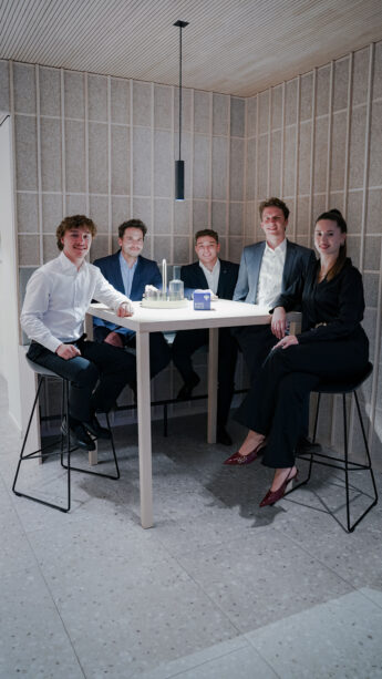 Vier Männer und eine Frau in Businesskleidung posieren lächelnd als junges Team in einem modernen Büro- bzw. Loungebereich.