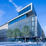 Frontansicht der Hypo Tirol Zentrale in Innsbruck, aufgenommen über den Bozner Platz mit Bäumen im Vordergrund.
