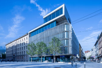 Frontansicht der Hypo Tirol Zentrale in Innsbruck, aufgenommen über den Bozner Platz mit Bäumen im Vordergrund.