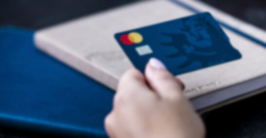 Hypo Debitkarte wird in Hand gehalten, dahinter ein Notizbuch.