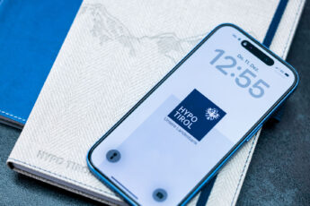 Smartphone mit Hypo Tirol Logo am Display liegt auf einem Notizbuch