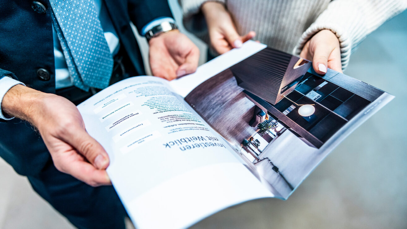 Kundin und Berater blättern gemeinsam durch eine Broschüre und Unterlagen.