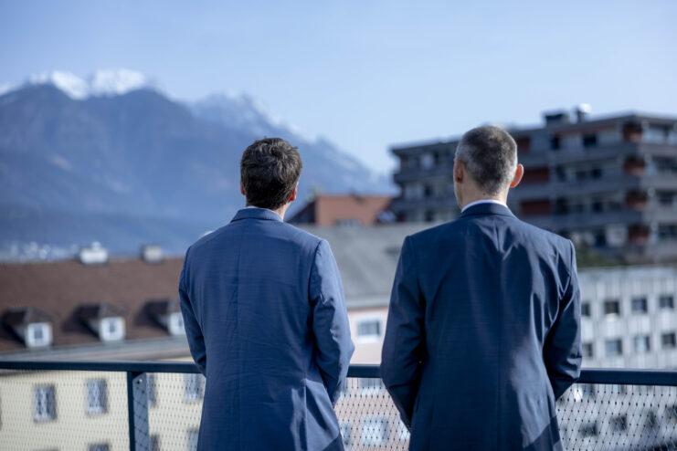 Zwei Mitarbeiter der Hypo Tirol im Gespräch auf einer Terrasse mit Blick auf die Tiroler Bergwelt.