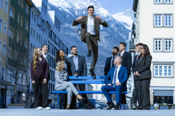 Gruppe von Personen im Freien vor einem Gebäude, eine Person befindet sich in Bewegung über dem Boden.