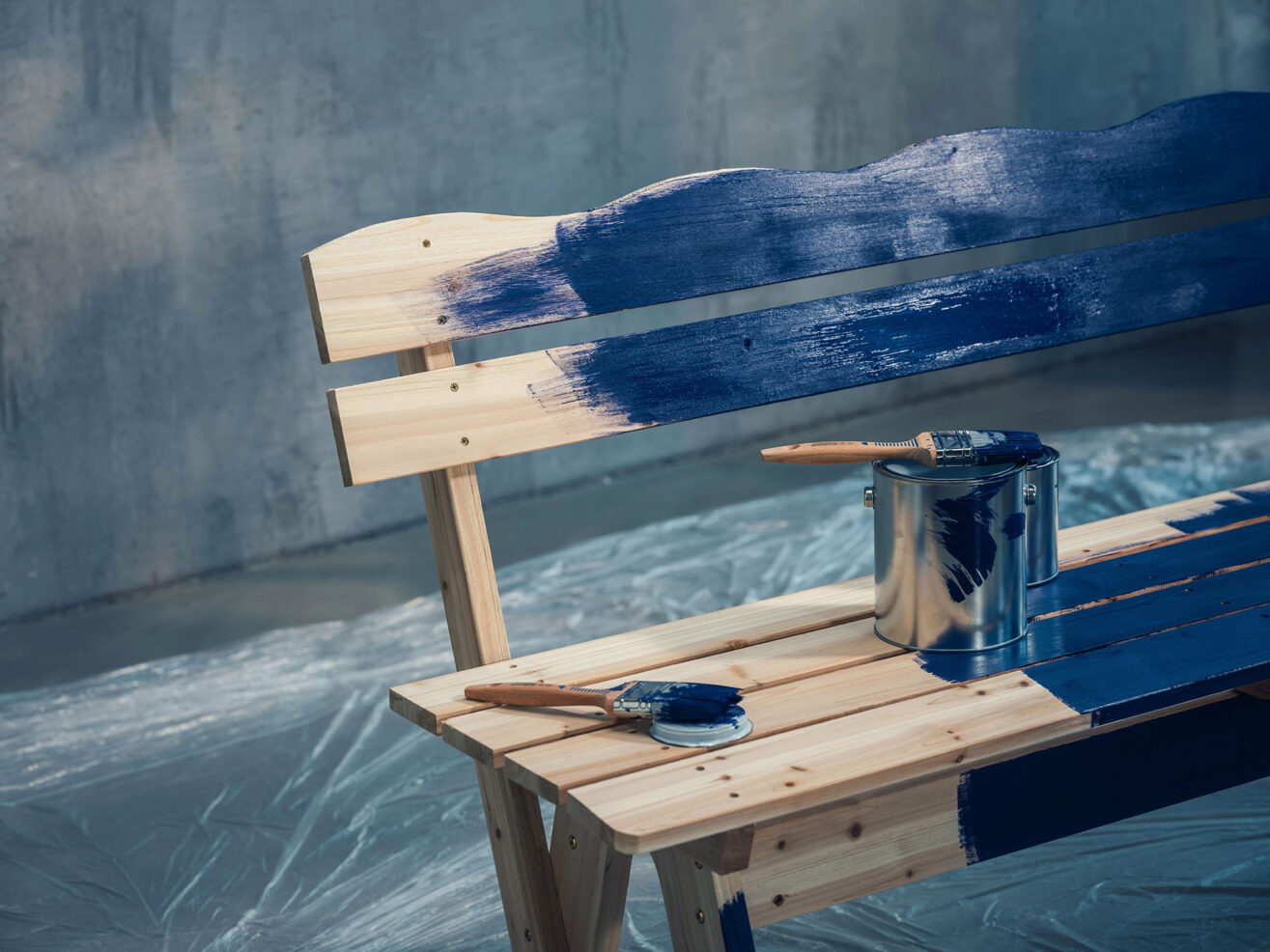 Detailaufnahme einer Holzbank, auf deren Rückenlehne blaue Farbe aufgetragen wird.