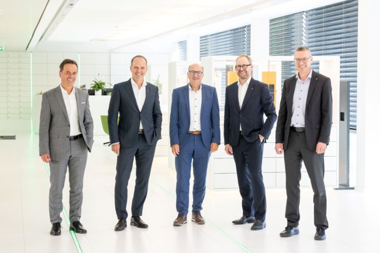 Gruppenfoto von fünf Personen beim Unternehmensbesuch bei Fiegl & Spielberger in einem modernen Büro- und Ausstellungsbereich.