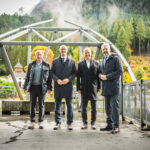 Vier Personen auf der Plattform einer Seilbahnanlage in Ehrwald in Tirol. Die Aufnahme zeigt die technische Infrastruktur der Anlage vor einer herbstlichen Berg- und Waldlandschaft.