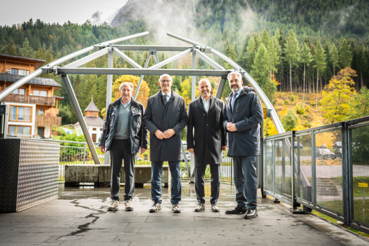 Vier Personen auf der Plattform einer Seilbahnanlage in Ehrwald in Tirol. Die Aufnahme zeigt die technische Infrastruktur der Anlage vor einer herbstlichen Berg- und Waldlandschaft.