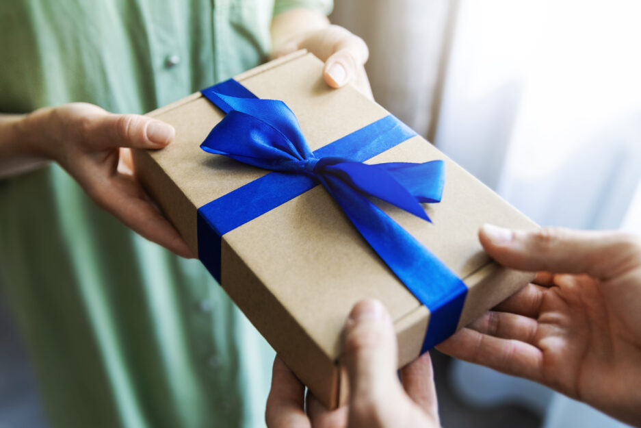 Mann übergibt eine Geschenkbox mit einer blauen Schleife an eine FraU