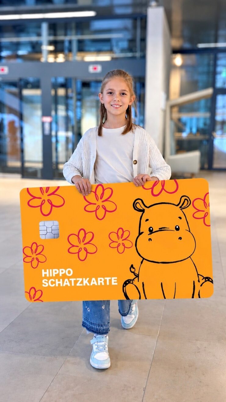 Kind hält die orange Hippo Schatzkarte in den Händen. Es lacht dabei.